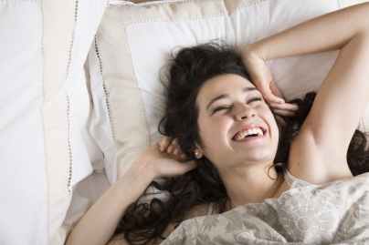 Woman-smiling-as-she-wakes-up-in-the-morning-000058977630_Medium